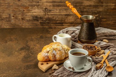 Kahve ve kruvasan, günaydın ve kahvaltı konsepti. Kahveli bakır Türk, sütlü sürahi, kahve çekirdekleri. Kahverengi taş arkaplan, kopyalama alanı