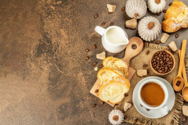 Bir fincan kahve, kruvasan, süt sürahisi ve dekoratif tığ işi balkabağı ile kahvaltı kavramı. Sıcak kahverengi taş zemin beton, üst görünüm