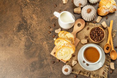 Bir fincan kahve, kruvasan, süt sürahisi ve dekoratif tığ işi balkabağı ile kahvaltı kavramı. Sıcak kahverengi taş zemin beton, üst görünüm