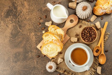 Bir fincan kahve, kruvasan, süt sürahisi ve dekoratif tığ işi balkabağı ile kahvaltı kavramı. Sıcak kahverengi taş zemin beton, üst görünüm