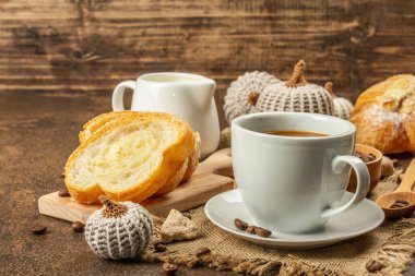 Bir fincan kahve, kruvasan, süt sürahisi ve dekoratif tığ işi balkabağı ile kahvaltı kavramı. Sıcak, kahverengi, beton arka plan, kapat.