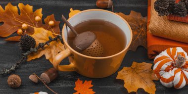 Bir fincan çay, el yapımı kumaş balkabakları, meşe palamutları, kozalakları, el sanatları için dökülen yapraklar ve tekstil ile rahat bir sonbahar hayatı, yavaş yaşam ve mevsimsel rahatlığı sembolize eder, afiş formatı