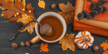 Bir fincan çay, el yapımı kumaş balkabakları, meşe palamutları, kozalakları, el sanatları için dökülen yapraklar ve tekstil ile rahat bir sonbahar hayatı, yavaş yaşam ve mevsimsel rahatlığı sembolize eder, afiş formatı