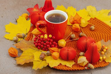 Sonbahar, bir fincan kırmızı çay, viburum üzümleri, meşe palamudu, sarı akçaağaç yaprakları ve sıcacık tonlarda el yapımı dekorlarla yavaş yaşam ve el yapımı konforu sembolize eder.