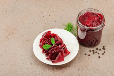 Cam bir kavanozda ve tabakta fermente pancar dilimleri. Ev yapımı, probiyotik zengini, vejetaryen ve mide sağlığı için sağlıklı beslenme. Açık kahverengi beton arkaplan, kopyalama alanı