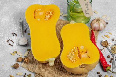 Zeytin yağı, deniz tuzu, biber ve kırmızı biberli yarım tereyağlı kabak. Vejetaryen sağlıklı beslenme, sonbahar hasadı, çiftlikten sofraya yemek pişirme, hafif taş arka plan, kapat.