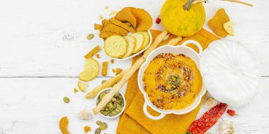 Tohumlar ve baharatlarla süslenmiş bir kase balkabağı humusu, Grissini ve kumaş peçetede kızarmış ekmeklerle servis ediliyor. Beyaz tahta tahtalar, vejetaryen sağlıklı gıda konsepti, afiş formatı