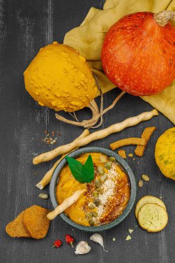 Vejetaryen balkabağı humusu rahatlatıcı bir mevsimlik aperatif olarak sunuldu. Siyah ahşap arka planda taze otlar, acı biber ve sarımsak.