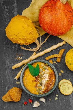 Vejetaryen balkabağı humusu rahatlatıcı bir mevsimlik aperatif olarak sunuldu. Siyah ahşap arka planda taze otlar, acı biber ve sarımsak.