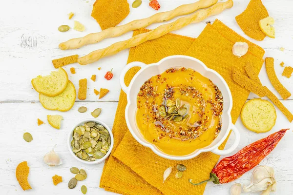 Tohumlar ve baharatlarla süslenmiş bir kase balkabağı humusu, Grissini ve kumaş peçetede kızarmış ekmeklerle servis ediliyor. Beyaz ahşap tahtalar, vejetaryen sağlıklı gıda konsepti, üst manzara.