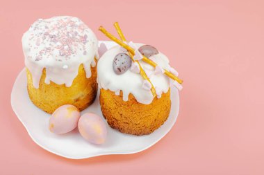 Geleneksel Paskalya pastaları, beyaz kremalı ve tabakta renkli yumurtalar serpiştirilmiş. Pembe arka planda tavşanları ve laleleri olan şenlikli bir kompozisyon. Ev yapımı tatil pişirme konsepti, kopyalama alanı