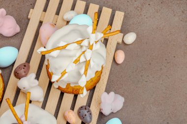 Traditional Easter cakes with white frosting and decorative pussy willow branches on wooden stand. Festive still life with pastel eggs and bunny figures on stone background, top view