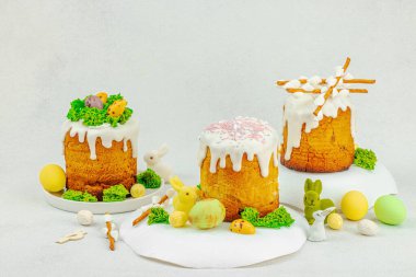 Beyaz kremalı Paskalya pastası, yosun süslemesi ve beyaz tabakta bıldırcın yumurtası. Renkli tavşancıkları ve açık gri arka planda yenilebilir söğüt dalları olan neşeli bahar kompozisyonu, boşluğu kopyala