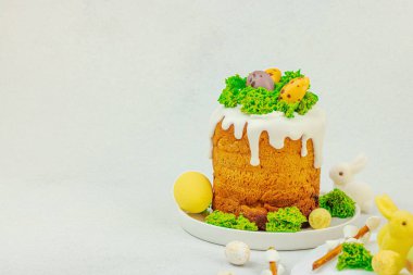 Beyaz kremalı Paskalya pastası, yosun süslemesi ve beyaz tabakta bıldırcın yumurtası. Renkli tavşancıkları ve açık gri arka planda yenilebilir söğüt dalları olan neşeli bahar kompozisyonu, boşluğu kopyala