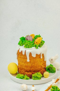 Beyaz kremalı Paskalya pastası, yosun süslemesi ve beyaz tabakta bıldırcın yumurtası. Renkli tavşancıkları ve açık gri arka planda yenilebilir söğüt dalları olan neşeli bahar kompozisyonu, boşluğu kopyala