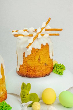 Beyaz kremalı Paskalya pastası, yosun süslemesi ve beyaz tabakta bıldırcın yumurtası. Renkli tavşancıkları ve açık gri arka planda yenilebilir söğüt dalları olan neşeli bahar kompozisyonu, boşluğu kopyala