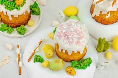 Beyaz kremalı Paskalya pastası, yosun süslemesi ve beyaz tabakta bıldırcın yumurtası. Renkli tavşancıklar ve açık gri arka planda yenilebilir söğüt dallarıyla şenlikli bahar kompozisyonu.