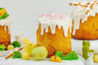 Beyaz kremalı Paskalya pastası, yosun süslemesi ve beyaz tabakta bıldırcın yumurtası. Renkli tavşancıklar ve açık gri arka planda yenilebilir söğüt dallarıyla şenlikli bahar kompozisyonu.