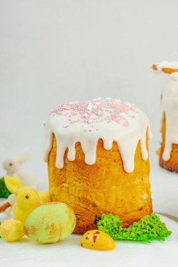 Beyaz kremalı Paskalya pastası, yosun süslemesi ve beyaz tabakta bıldırcın yumurtası. Renkli tavşancıklar ve açık gri arka planda yenilebilir söğüt dallarıyla şenlikli bahar kompozisyonu.