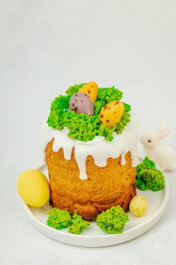 Beyaz kremalı Paskalya pastası, yosun süslemesi ve beyaz tabakta bıldırcın yumurtası. Renkli tavşancıklar ve açık gri arka planda yenilebilir söğüt dallarıyla şenlikli bahar kompozisyonu.