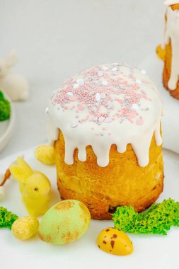 Beyaz kremalı Paskalya pastası, yosun süslemesi ve beyaz tabakta bıldırcın yumurtası. Renkli tavşancıklar ve açık gri arka planda yenilebilir söğüt dallarıyla şenlikli bahar kompozisyonu.