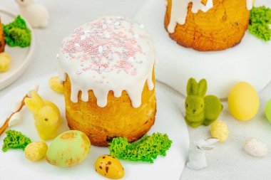 Beyaz kremalı Paskalya pastası, yosun süslemesi ve beyaz tabakta bıldırcın yumurtası. Renkli tavşancıklar ve açık gri arka planda yenilebilir söğüt dallarıyla şenlikli bahar kompozisyonu.