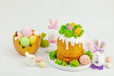 Beyaz kremalı Paskalya pastası, yosun süslemesi ve beyaz tabakta bıldırcın yumurtası. Renkli tavşancıkları ve açık gri arka planda yenilebilir söğüt dalları olan neşeli bahar kompozisyonu, boşluğu kopyala