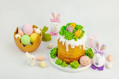 Beyaz kremalı Paskalya pastası, yosun süslemesi ve beyaz tabakta bıldırcın yumurtası. Renkli tavşancıkları ve açık gri arka planda yenilebilir söğüt dalları olan neşeli bahar kompozisyonu, boşluğu kopyala