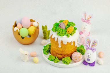 Beyaz kremalı Paskalya pastası, yosun süslemesi ve beyaz tabakta bıldırcın yumurtası. Renkli tavşancıkları ve açık gri arka planda yenilebilir söğüt dalları olan neşeli bahar kompozisyonu, boşluğu kopyala