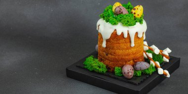 Yenilebilir yosun yuvası, çikolata yumurtası ve el yapımı söğüt dallarıyla süslenmiş Paskalya pastası. Siyah taş zemin üzerinde tavşan figürleri olan geleneksel şenlikli tatlı, afiş biçimi