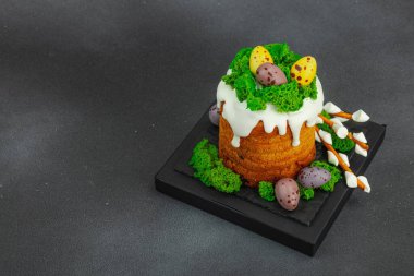 Yenilebilir yosun yuvası, çikolata yumurtası ve el yapımı söğüt dallarıyla süslenmiş Paskalya pastası. Siyah taş zemin üzerinde tavşan figürleri olan geleneksel şenlikli tatlı, kopyalama alanı