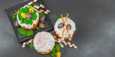 Yenilebilir yosun yuvası, çikolata yumurtası ve el yapımı söğüt dallarıyla süslenmiş paskalya pastaları. Siyah taş zemin üzerinde tavşan figürleri olan geleneksel şenlikli tatlı, afiş biçimi