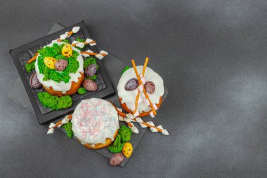 Yenilebilir yosun yuvası, çikolata yumurtası ve el yapımı söğüt dallarıyla süslenmiş paskalya pastaları. Siyah taş arka planda tavşan figürlü geleneksel şenlikli tatlı.