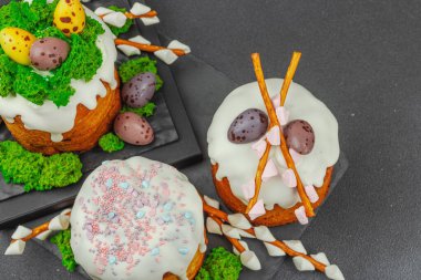 Yenilebilir yosun yuvası, çikolata yumurtası ve el yapımı söğüt dallarıyla süslenmiş paskalya pastaları. Siyah taş arka planda tavşan figürlü geleneksel şenlikli tatlı.