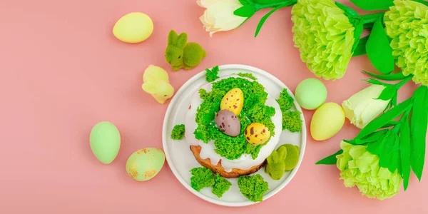 Geleneksel Paskalya pastaları, beyaz kremalı ve tabakta renkli yumurtalar serpiştirilmiş. Pembe arka planda tavşanlı ve çiçekli şenlikli kompozisyon. Ev yapımı tatil pişirme konsepti, afiş biçimi