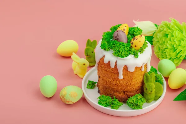 Geleneksel Paskalya pastaları, beyaz kremalı ve tabakta renkli yumurtalar serpiştirilmiş. Pembe arka planda tavşanlı ve çiçekli şenlikli kompozisyon. Ev yapımı tatil pişirme konsepti, kopyalama alanı
