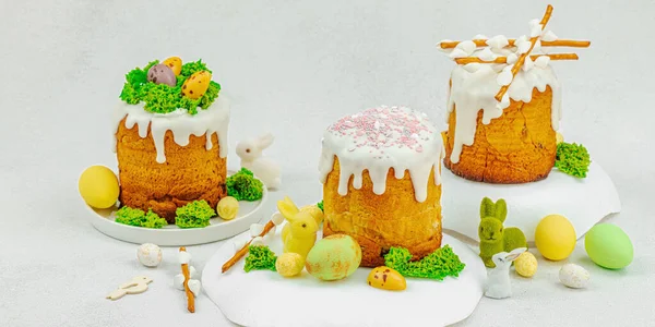 Beyaz kremalı Paskalya pastası, yosun süslemesi ve beyaz tabakta bıldırcın yumurtası. Renkli tavşancıklar ve açık gri arka planda yenilebilir söğüt dalları ve pankart formatlı şenlikli bahar kompozisyonu