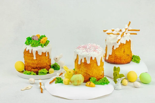 Beyaz kremalı Paskalya pastası, yosun süslemesi ve beyaz tabakta bıldırcın yumurtası. Renkli tavşancıkları ve açık gri arka planda yenilebilir söğüt dalları olan neşeli bahar kompozisyonu, boşluğu kopyala