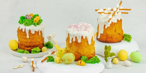 Beyaz kremalı Paskalya pastası, yosun süslemesi ve beyaz tabakta bıldırcın yumurtası. Renkli tavşancıklar ve açık gri arka planda yenilebilir söğüt dalları ve pankart formatlı şenlikli bahar kompozisyonu