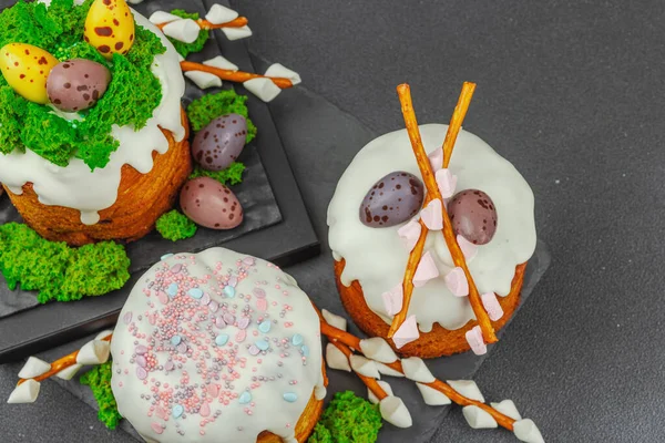 Yenilebilir yosun yuvası, çikolata yumurtası ve el yapımı söğüt dallarıyla süslenmiş paskalya pastaları. Siyah taş arka planda tavşan figürlü geleneksel şenlikli tatlı.
