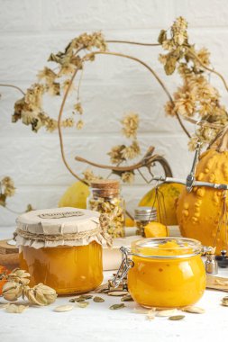 Antika eczacılık tarzında sağlıklı gıda konsepti. Ev yapımı kabak püresi ve beyaz ahşap bir masada cam kavanozlarda humus. Balkabağı, kurutulmuş zıpzıp ve bitki özü ile kırsal sonbahar natürmortu, kopyalama alanı