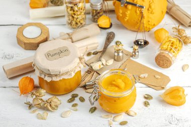 Antika eczacılık tarzında sağlıklı gıda konsepti. Ev yapımı kabak püresi ve beyaz ahşap bir masada cam kavanozlarda humus. Balkabağı, kurutulmuş zıpzıp ve bitki özü ile kırsal sonbahar natürmortu, kopyalama alanı