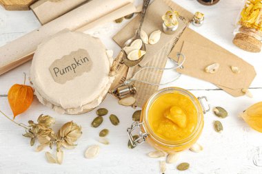 Antika eczacılık tarzında sağlıklı gıda konsepti. Ev yapımı kabak püresi ve beyaz ahşap bir masada cam kavanozlarda humus. Balkabağı, kurutulmuş zıpzıp ve bitki özü ile kırsal sonbahar natürmortu.