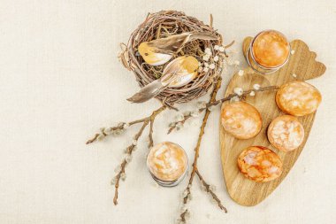 Easter eggs dyed with natural onion skins in a rustic setting with pussy willow branches, craft tools, and spring flowers. Traditional sustainable holiday decoration and process concept, top view