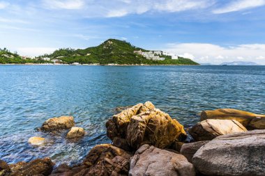 Hong Kong 'daki Hong Kong Adası' ndaki Stanley Körfezi 'nin Rocky sahili. Su, dağlar, kayalar, binalar, balıkçı tekneleri ve bulutlu gökyüzü ile güzel manzaralar.