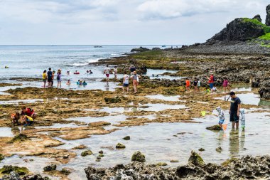 Turistler Pingtung, Tayvan 'daki Kenting Ulusal Parkı kıyısındaki gelgit bölgesini keşfediyorlar.