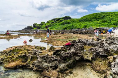 Turistler Pingtung, Tayvan 'daki Kenting Ulusal Parkı kıyısındaki gelgit bölgesini ziyaret ediyorlar..