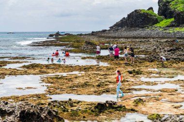 Turistler Pingtung, Tayvan 'daki Kenting Ulusal Parkı kıyısındaki gelgit bölgesini keşfediyorlar.