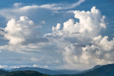 Mavi gökyüzü ve bulutlu yuvarlanan dağlar.