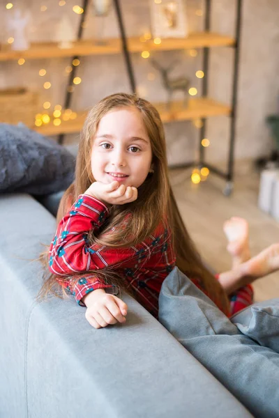 在睡衣里快乐的小女孩坐在现代客厅里灰色的沙发上 — 图库照片